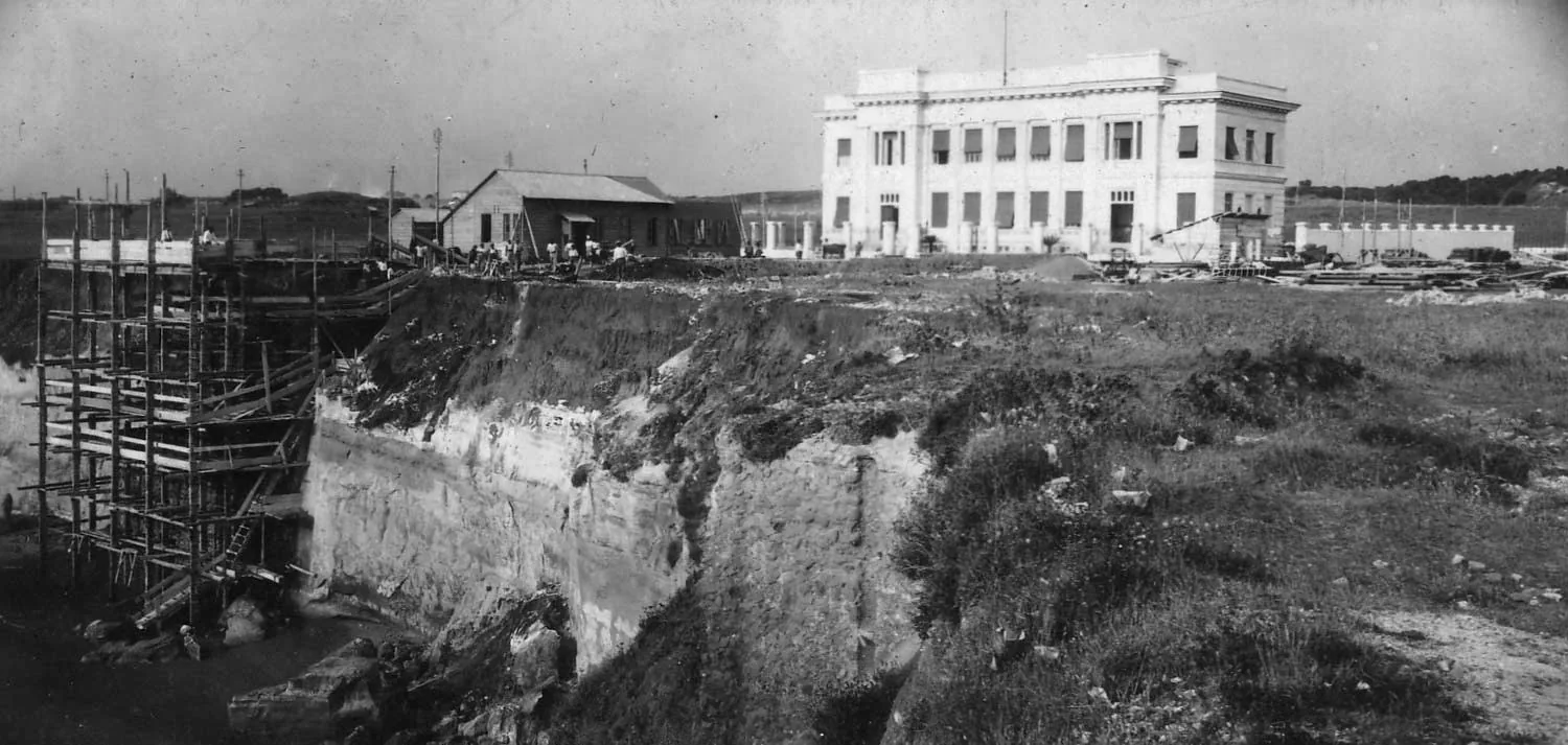 Foto storica in bianco e nero del sito di approdo del cavo Italcable ad Anzio: a sinistra la baracca del cavo con impalcature sul ciglio della scogliera, sullo sfondo la palazzina della Stazione