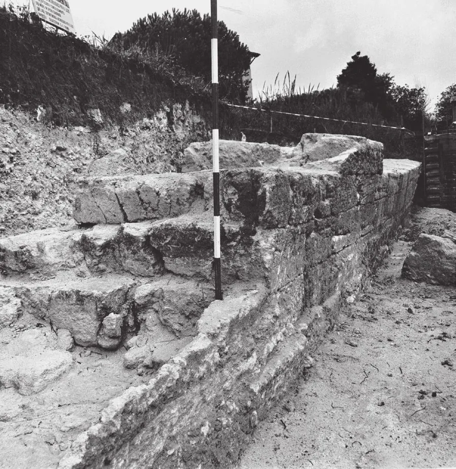 Fotografia del muro in opera quadrata di macco del Vallo di Antium messo in luce dagli scavi della Soprintendenza, con visibili i filari di blocchi e la piega del muro